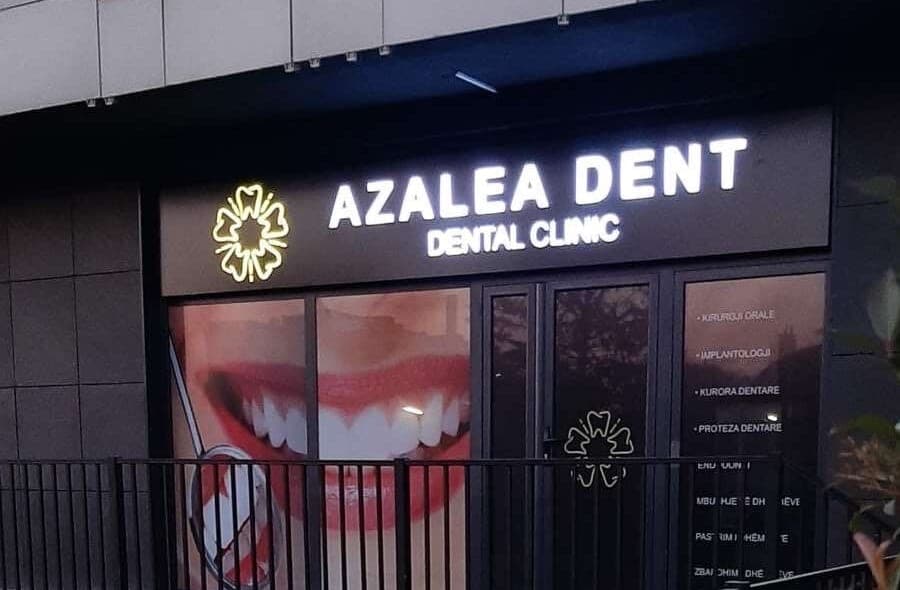 Hyrja e klinikës Azalea Dent në mbrëmje, me tabelën e ndriçuar dhe logon në formë lulëzimi azalea.
